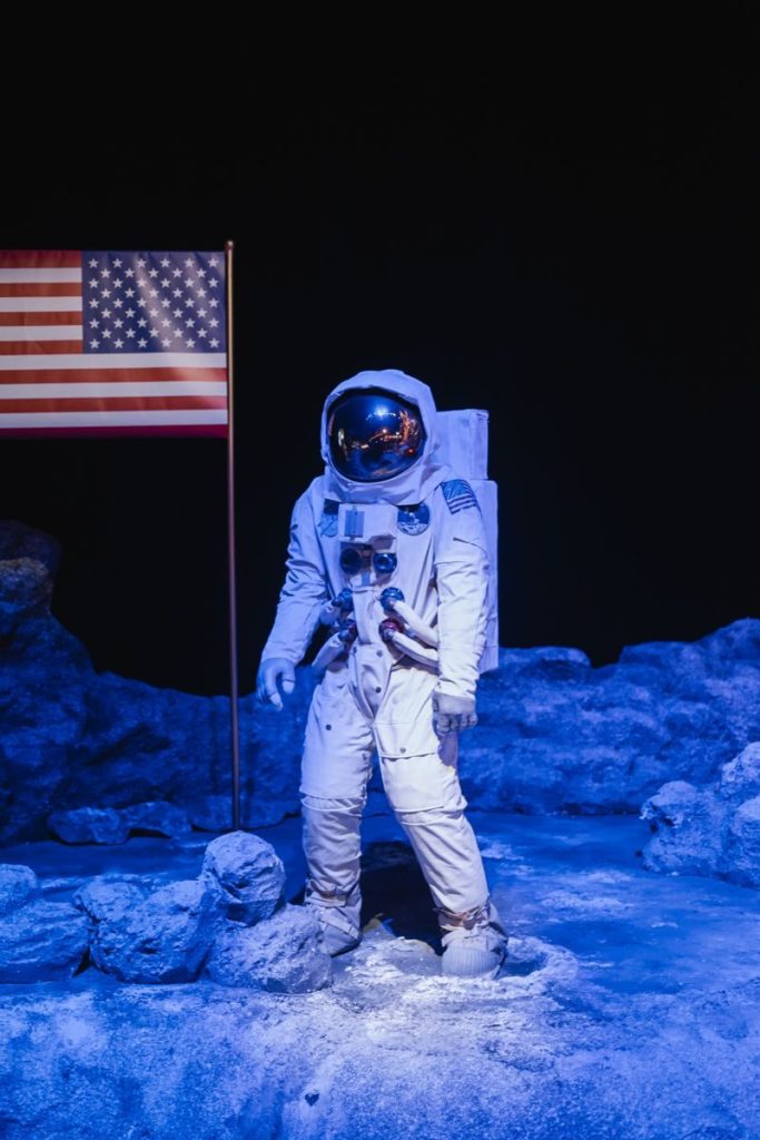 Astronaut in a space suit standing on a moon surface set with an American flag.