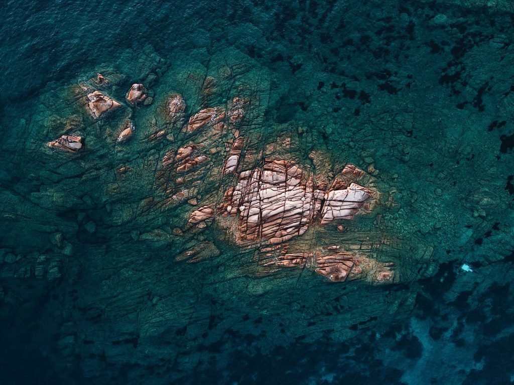 Stunning aerial view of rocky formation submerged in crystal-clear sea water, offering serene natural beauty.