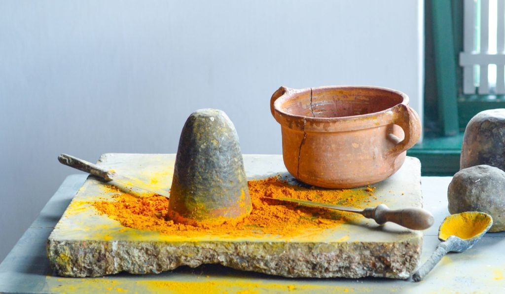 A rustic kitchen scene of traditional spice grinding with clay pot and spoon indoors.