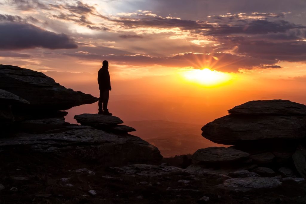A dramatic scene of a person standing on a rocky cliff during sunset.