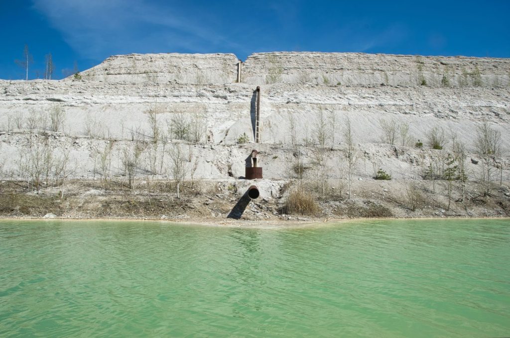 A serene view of a limestone quarry with clear turquoise water and a dramatic cliff face.