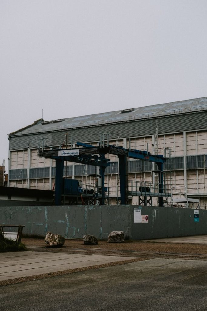 A large industrial crane positioned outside a shipping port warehouse on a cloudy day.