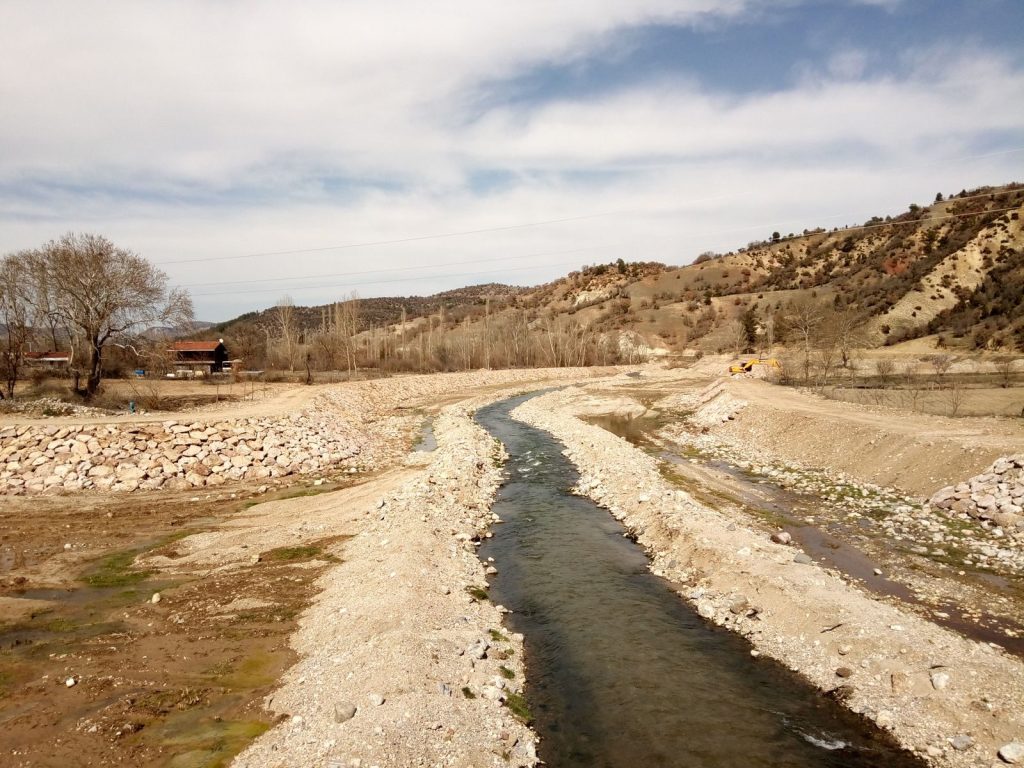 A peaceful stream winds through a rocky autumn landscape under a cloudy sky.