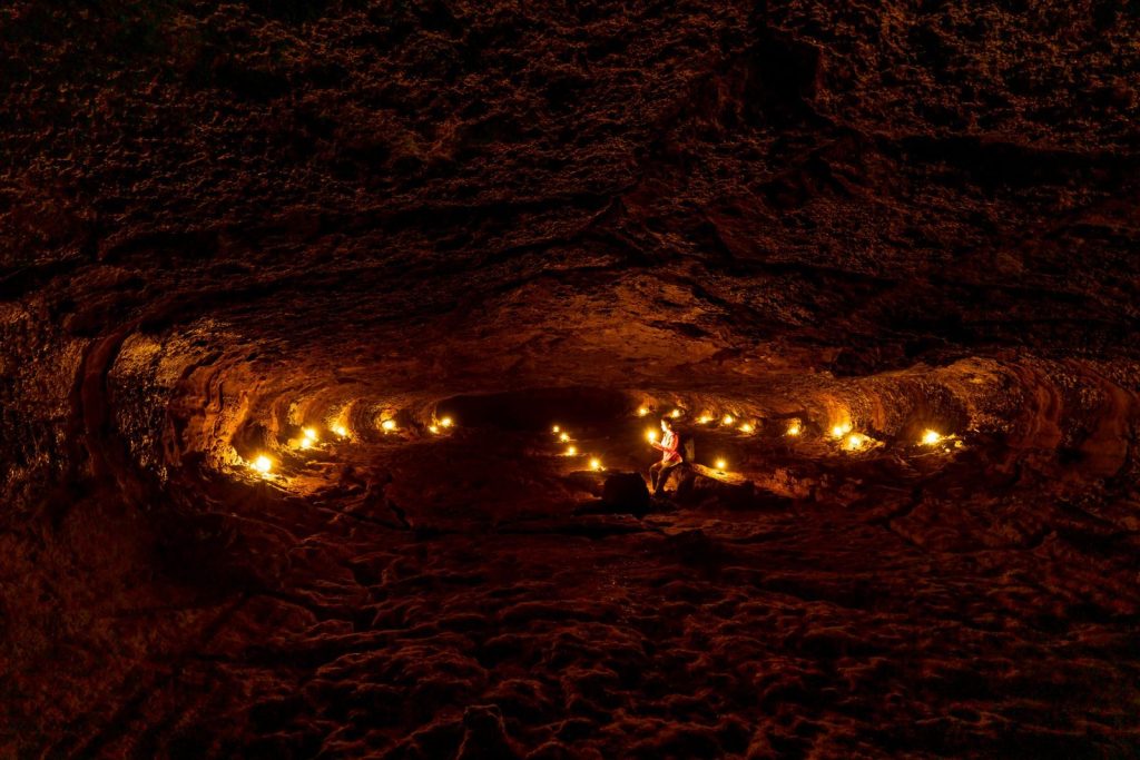 A person exploring a dimly lit cave with candles, showcasing natural rock formations.