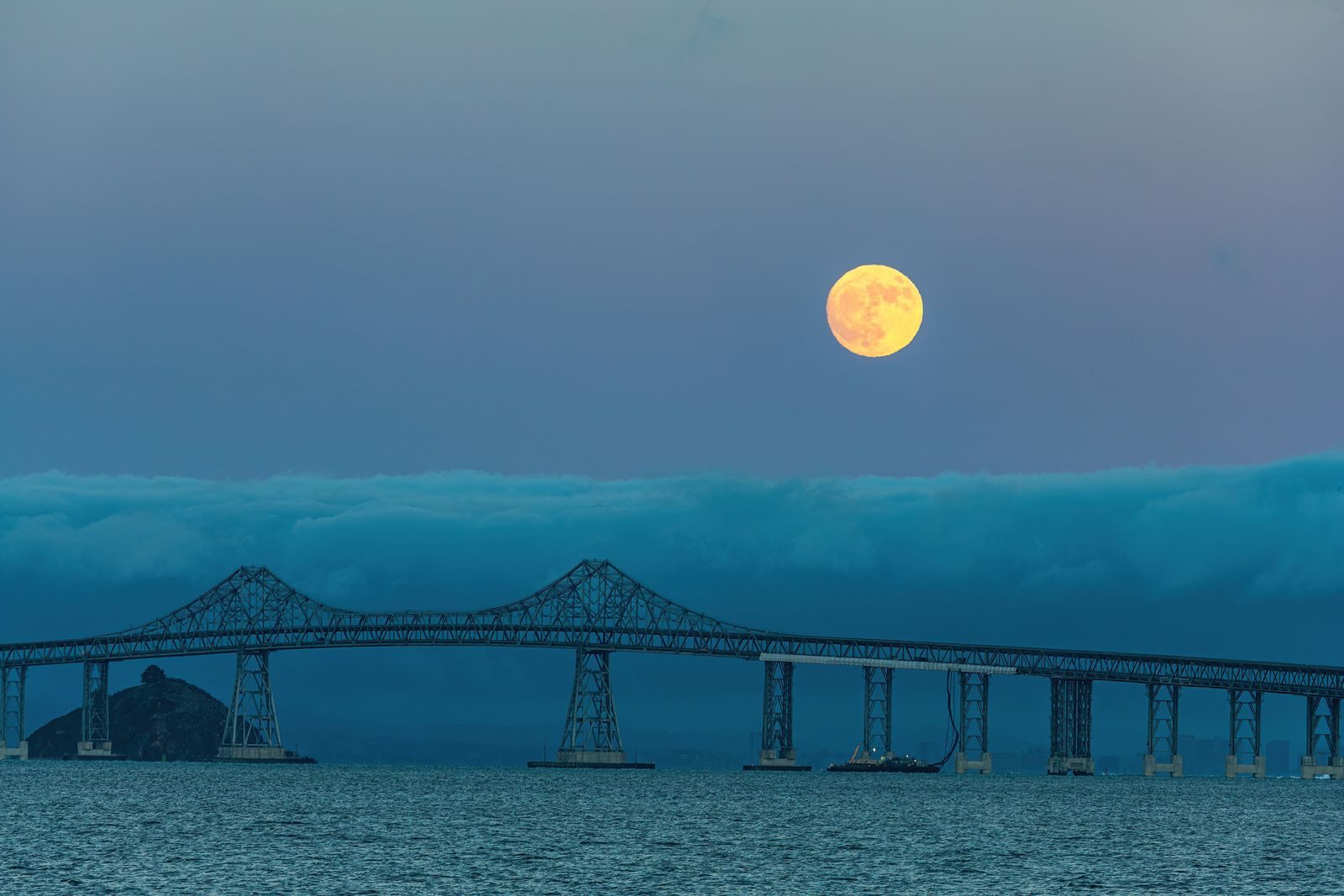 Stunning view of a full moon above a steel suspension bridge with ocean below.