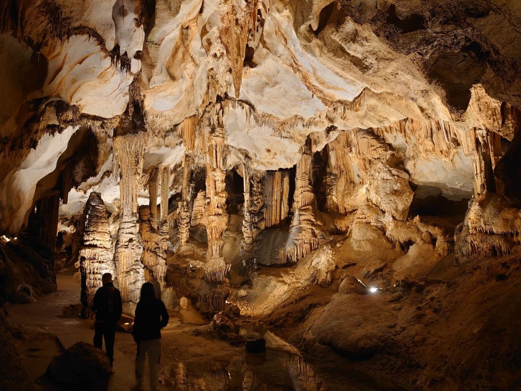 Dramatic stalactites and stalagmites in a limestone cave with two people exploring.