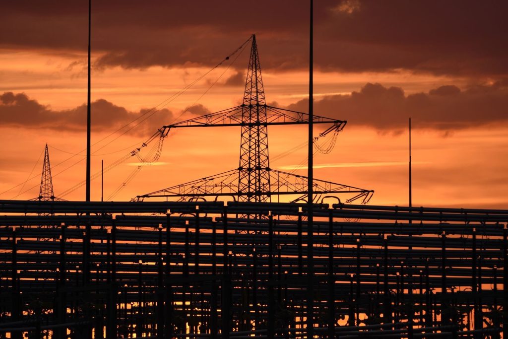 Silhouetted electric tower against vivid sunset sky, highlighting urban infrastructure.
