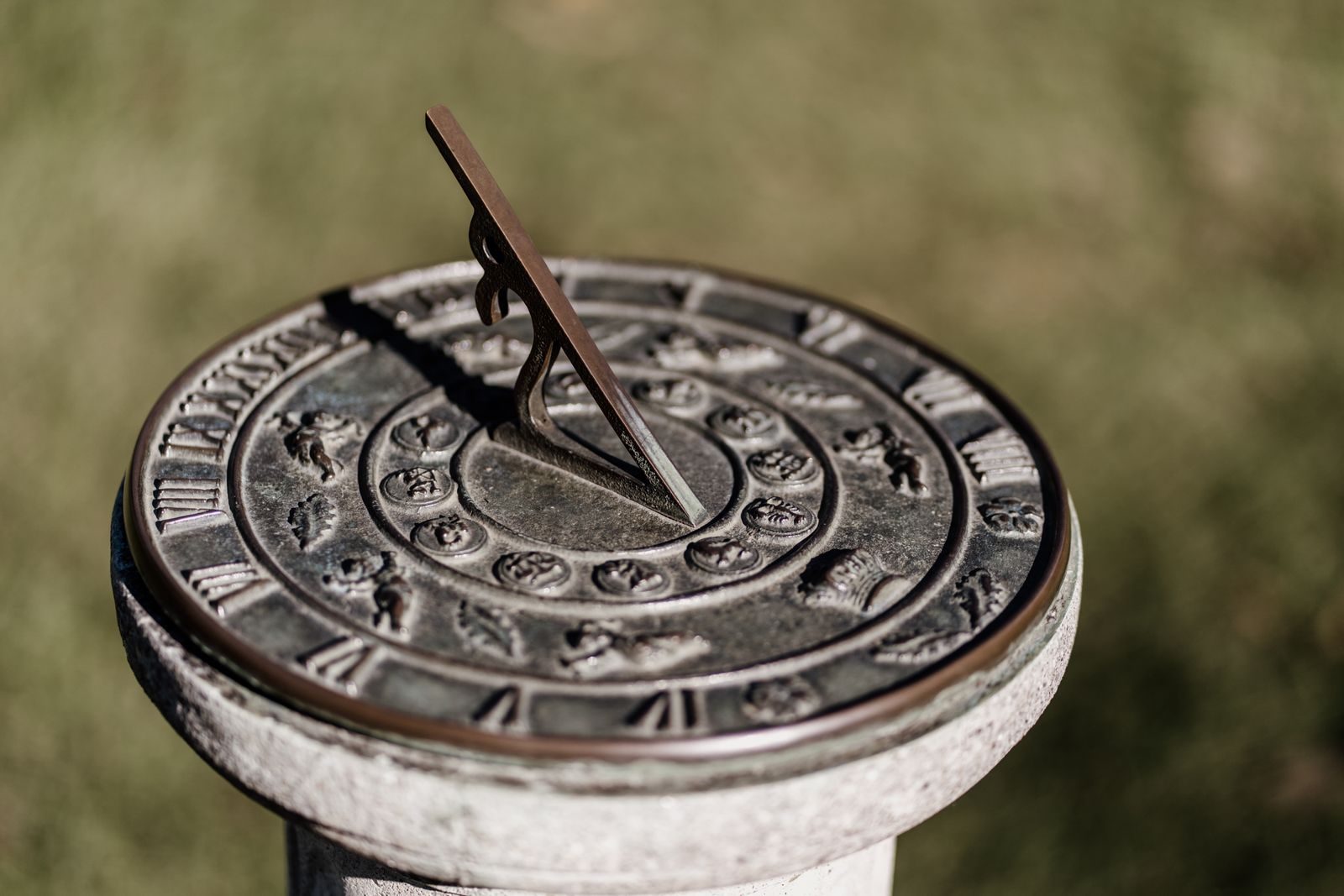 Close-up of a classic sundial with Roman numerals and zodiac signs in a garden.