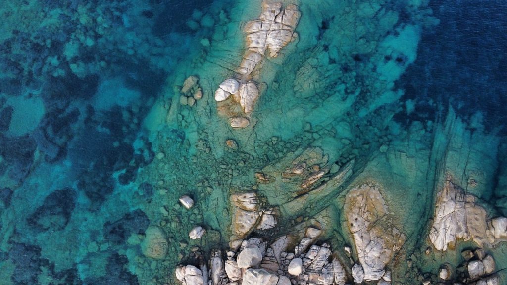 Drone shot capturing clear turquoise waters and rocky coastline from above.