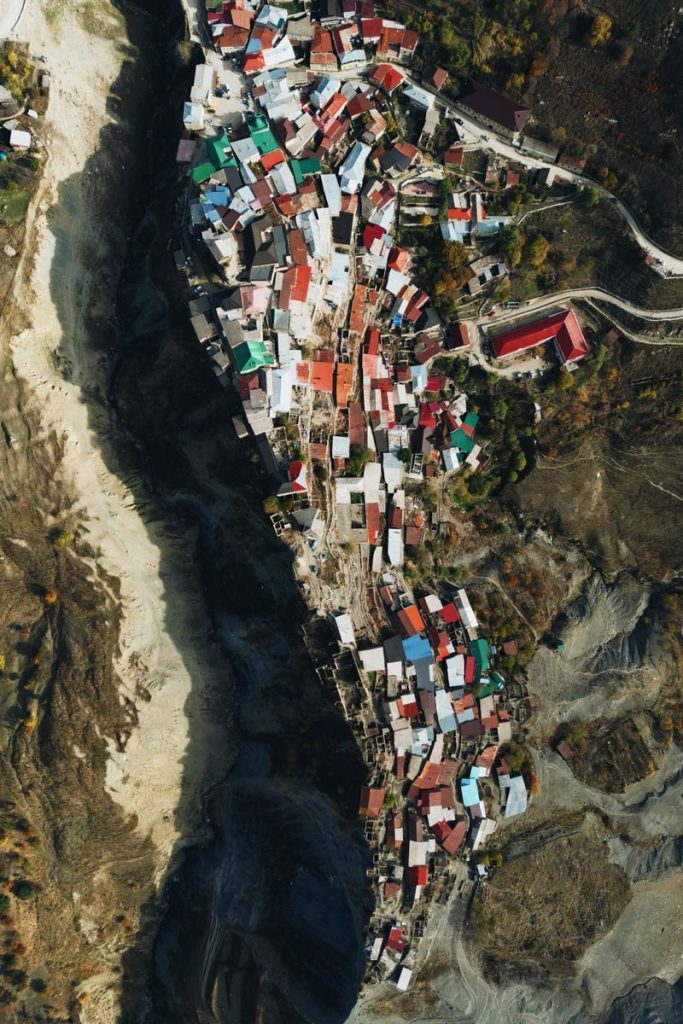 Bird's eye view of a colorful town nestled along a winding riverbank, showcasing diverse rooftops and dramatic landscape.