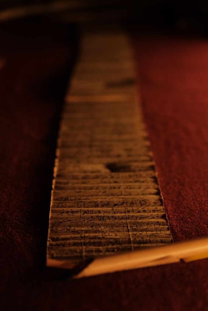 Close-up view of an ancient papyrus scroll, showcasing historic scripts, in a dimly lit museum setting.