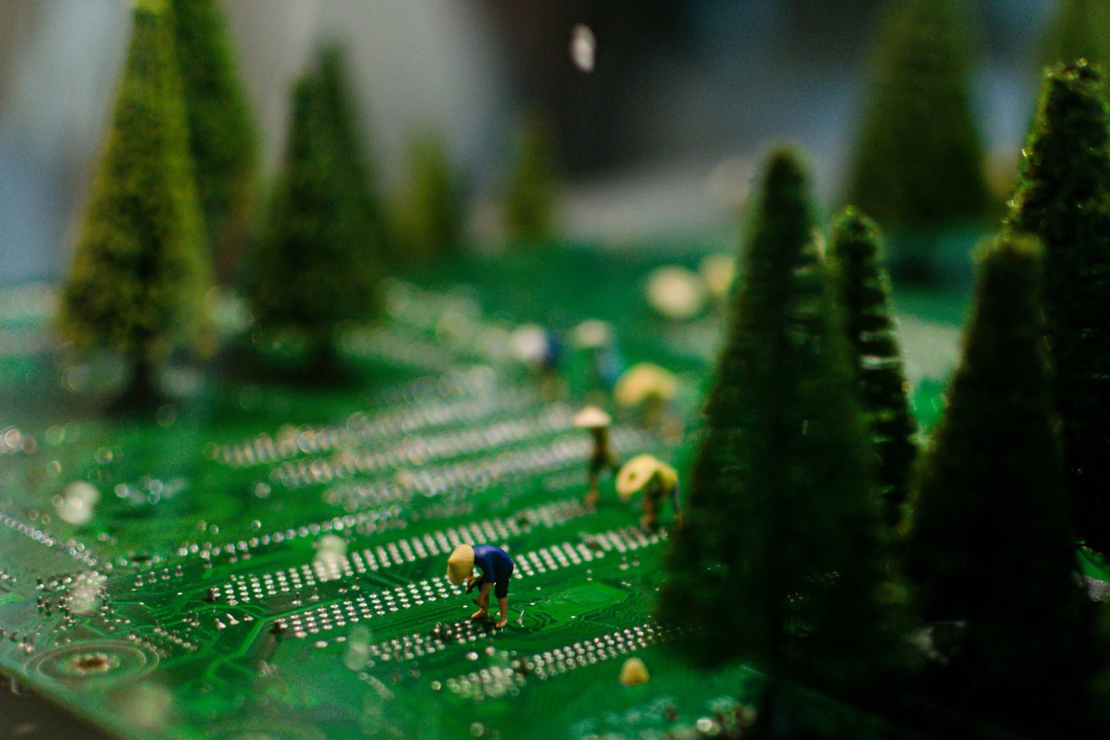 Creative scene of miniature figures farming on a circuit board with artificial trees.