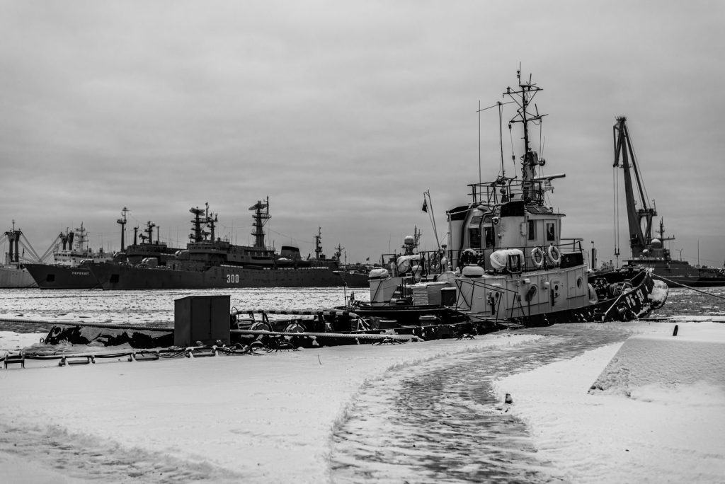 A snowy harbor with moored ships and boats in a dramatic black and white setting.
