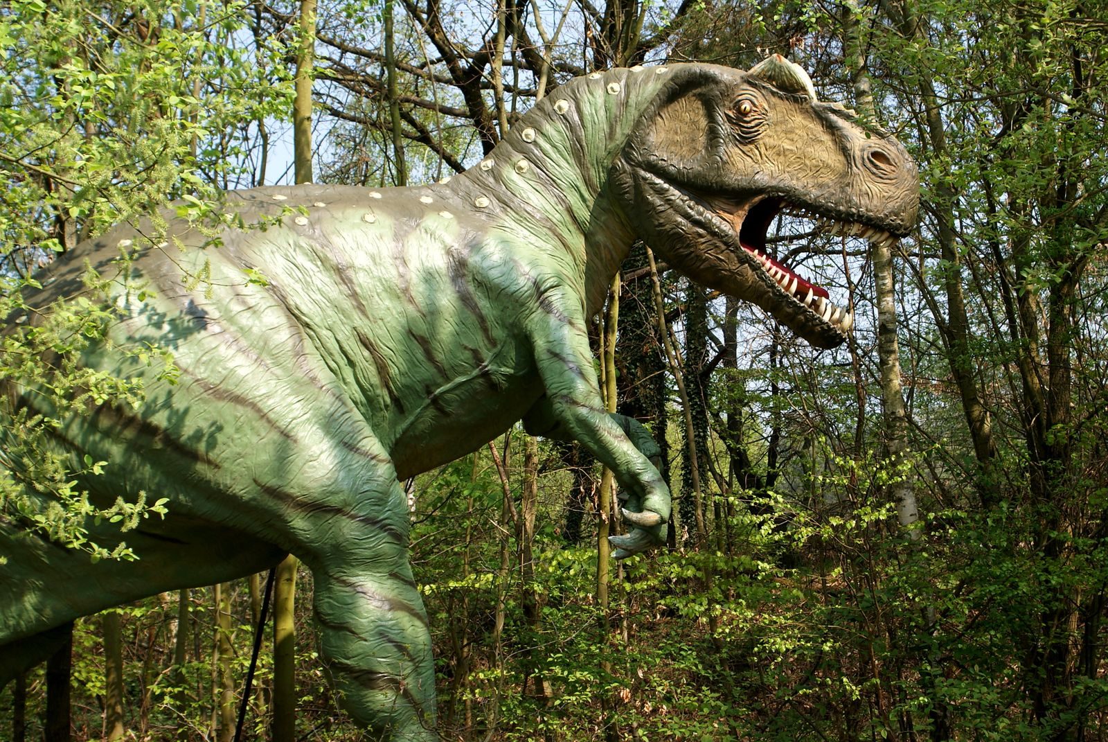 Large dinosaur statue amidst greenery in an outdoor theme park setting.