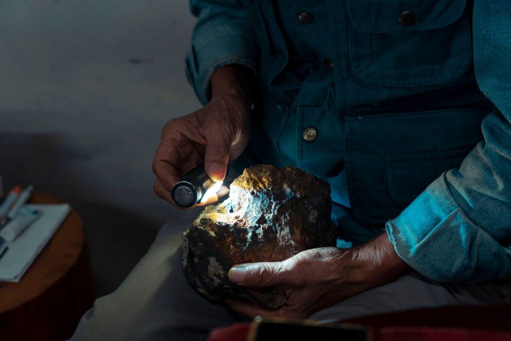 Detailed close-up of hands using a flashlight to examine a geological stone indoors.