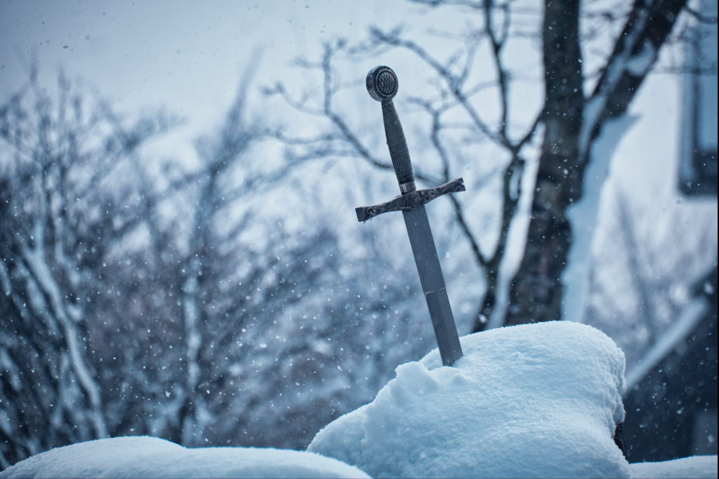 Close-up of a medieval sword embedded in snowy ground during winter.
