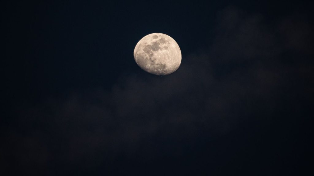 A clear view of the bright moon shining amidst dark clouds.