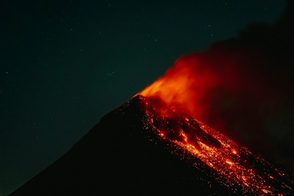 A volcano erupting at night with glowing lava and smoke.
