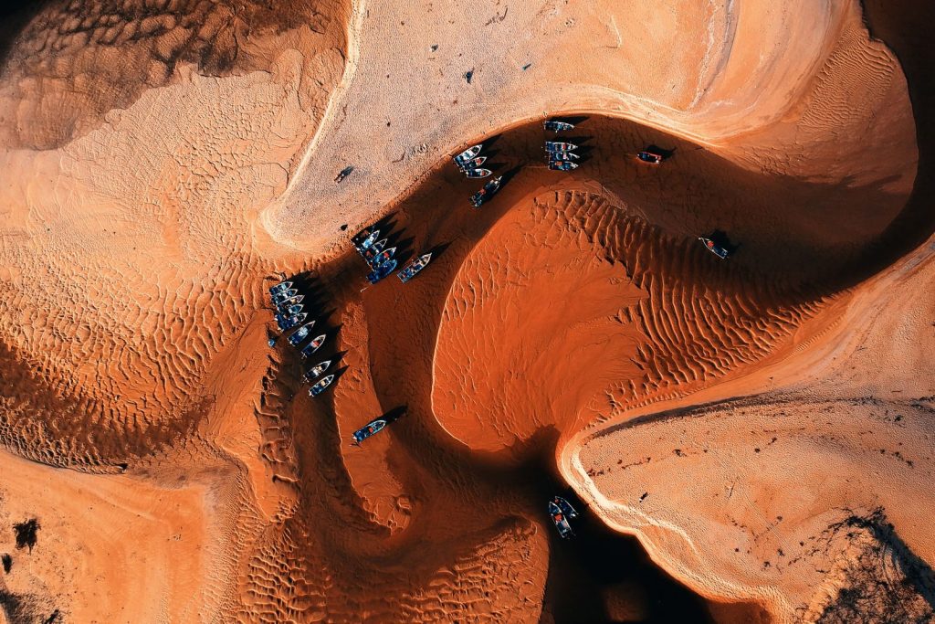 Stunning aerial view of arid terrain with boats on a dried riverbed, showcasing natural patterns.