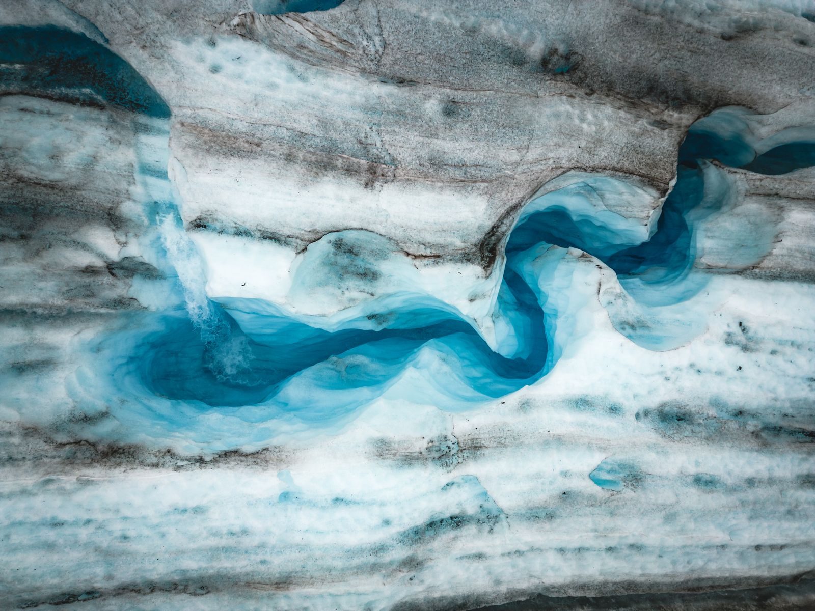 Stunning aerial view of a winding glacier with vibrant blue ice, capturing nature's artistry.