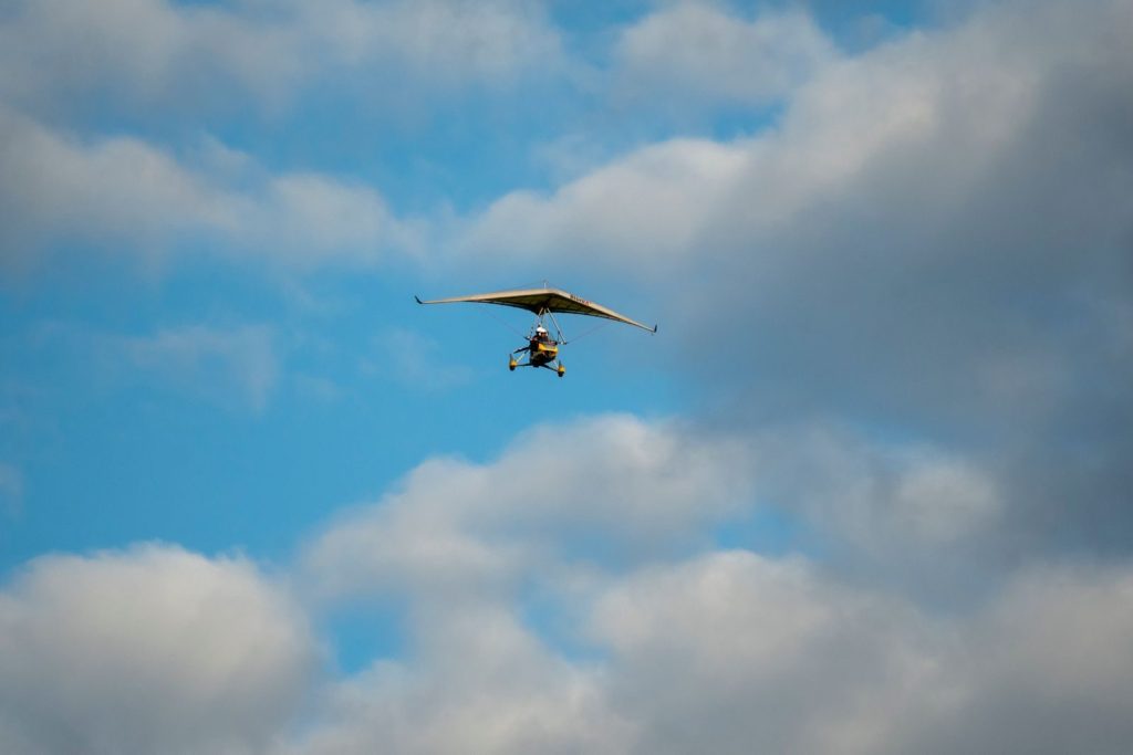 A hang glider soaring through the blue sky, surrounded by clouds, capturing a sense of freedom and adventure.