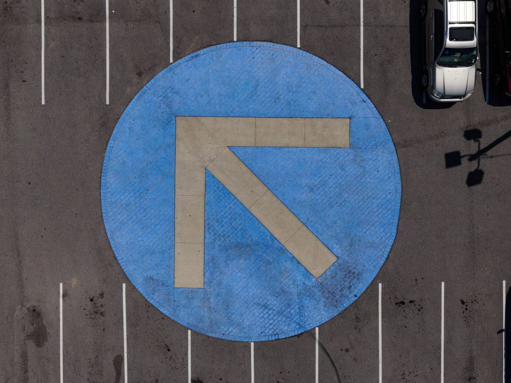 Top-down shot of a blue arrow traffic sign in a concrete parking area.