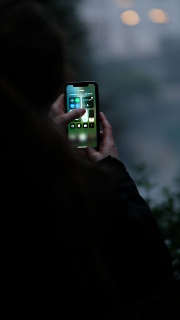 Close-up of hands using a smartphone outdoors in dim light conditions, perfect for tech and lifestyle themes.