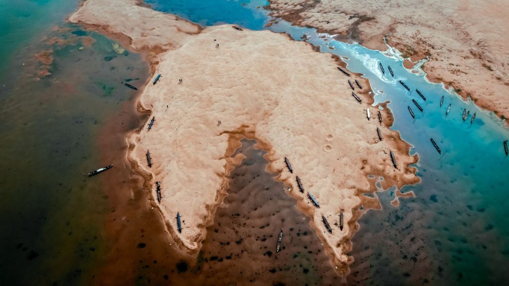 Aerial photograph showcasing a sandy island formation surrounded by clear blue water with boats scattered around.