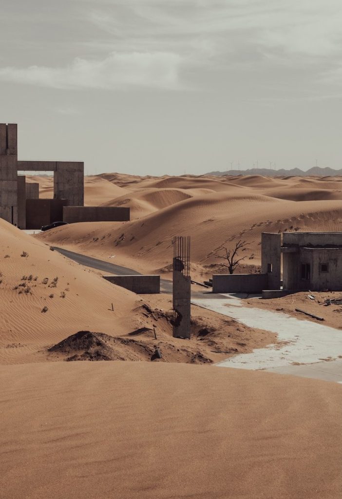 Abandoned concrete buildings buried in vast desert sand dunes.