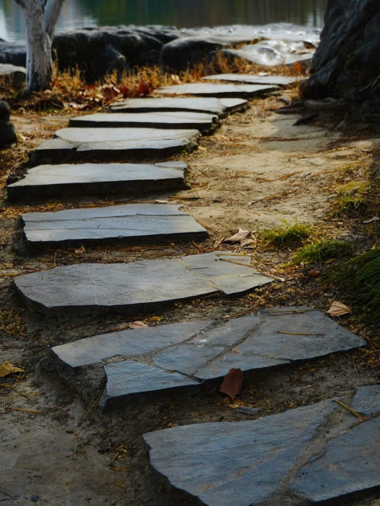 A rustic stone pathway leads through a serene garden setting, perfect for peace and reflection.