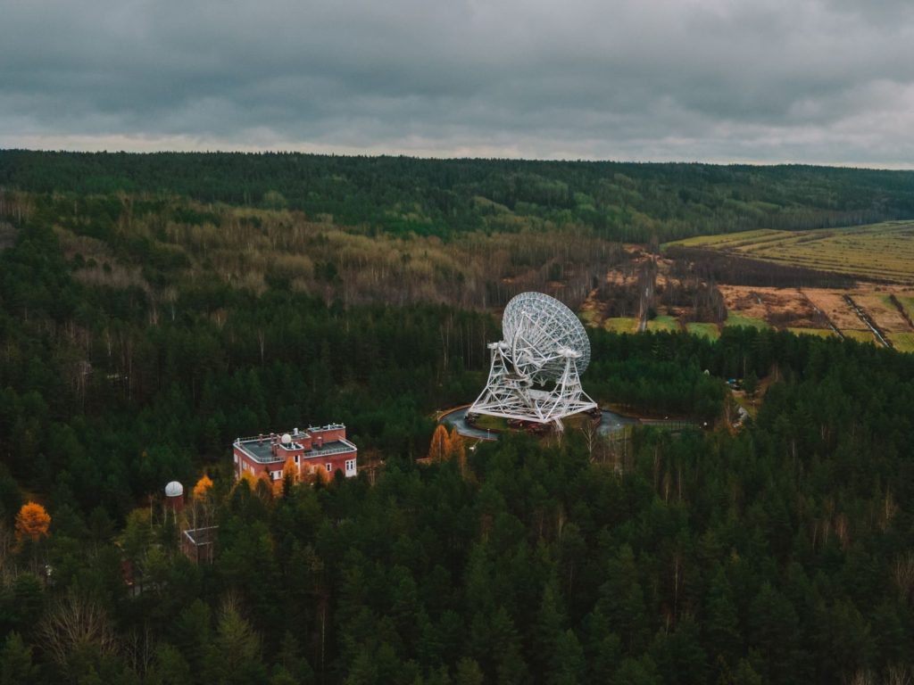Aerial view of a large telescope amid lush forest, highlighting nature and technology.