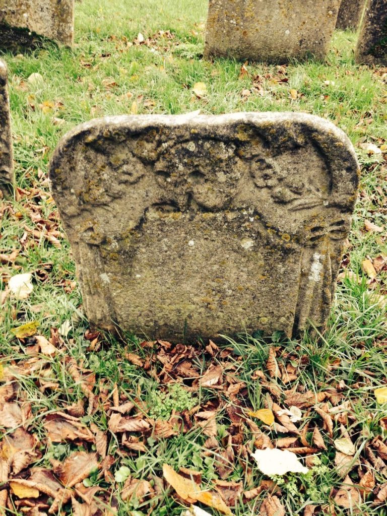 Old gravestone with angel carvings in a grassy cemetery, autumn leaves around.