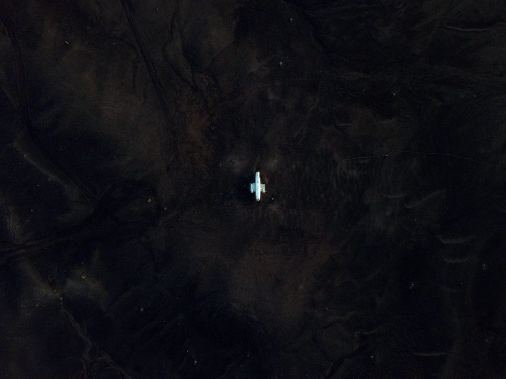 Aerial perspective of a solitary vehicle on dark, vast Icelandic landscape.