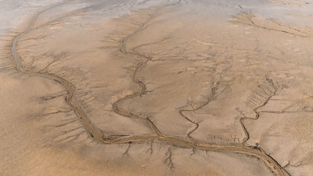 High-angle aerial view of barren desert terrain with dried riverbeds.