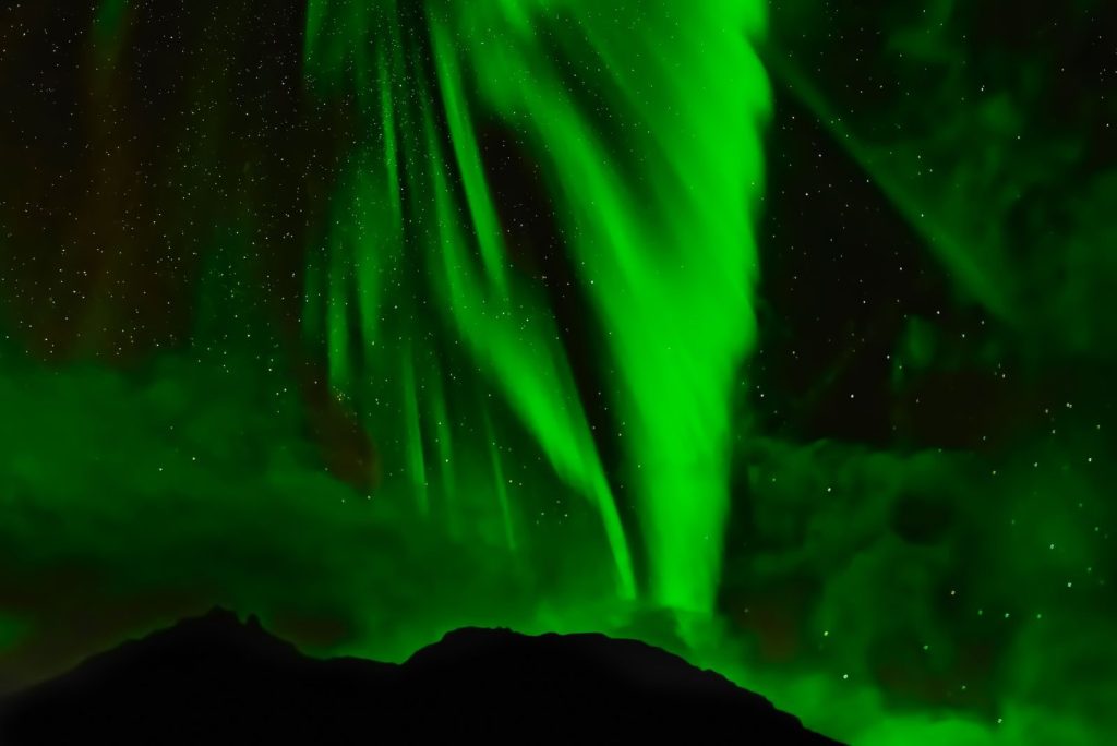 Captivating view of green aurora borealis lighting up the night sky above a mountain silhouette.