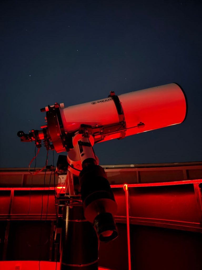 A telescope inside a red-lit observatory pointed at the night sky, capturing celestial views.