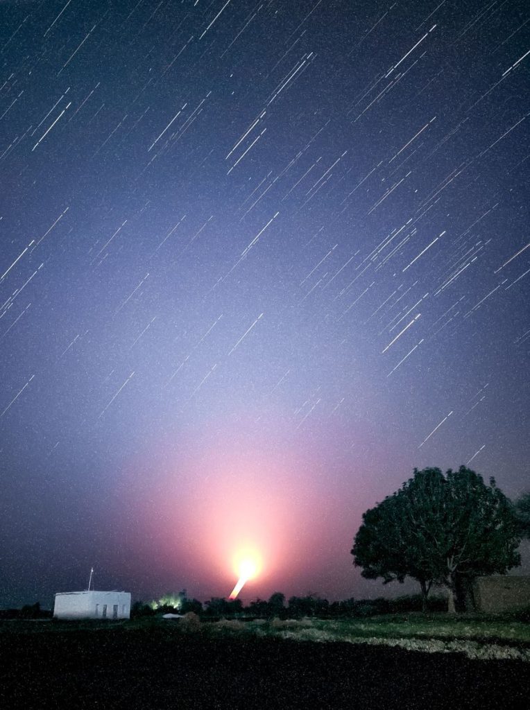 Long exposure photo capturing star trails and a bright glow over the landscape of Kandiāro, Sindh.