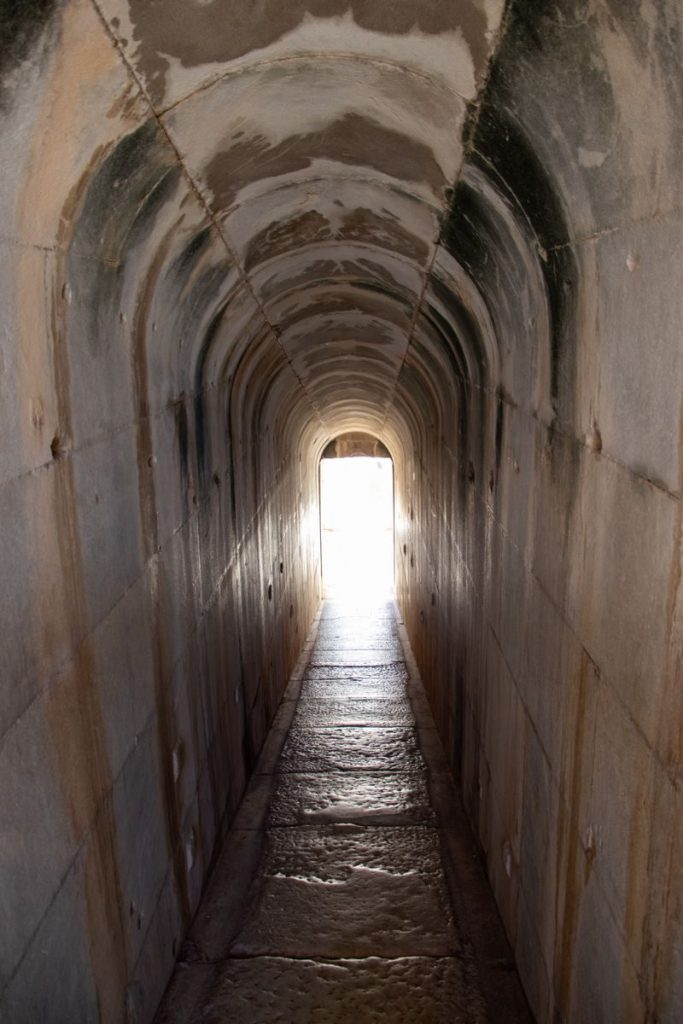 Explore a historic stone corridor leading to a bright exit, evoking mystery and intrigue.