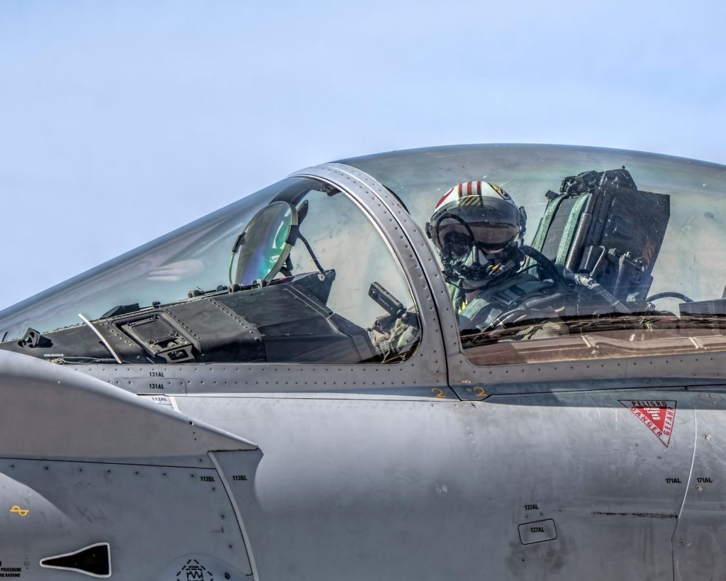 Close-up of a fighter jet pilot in the cockpit flying during a clear day.
