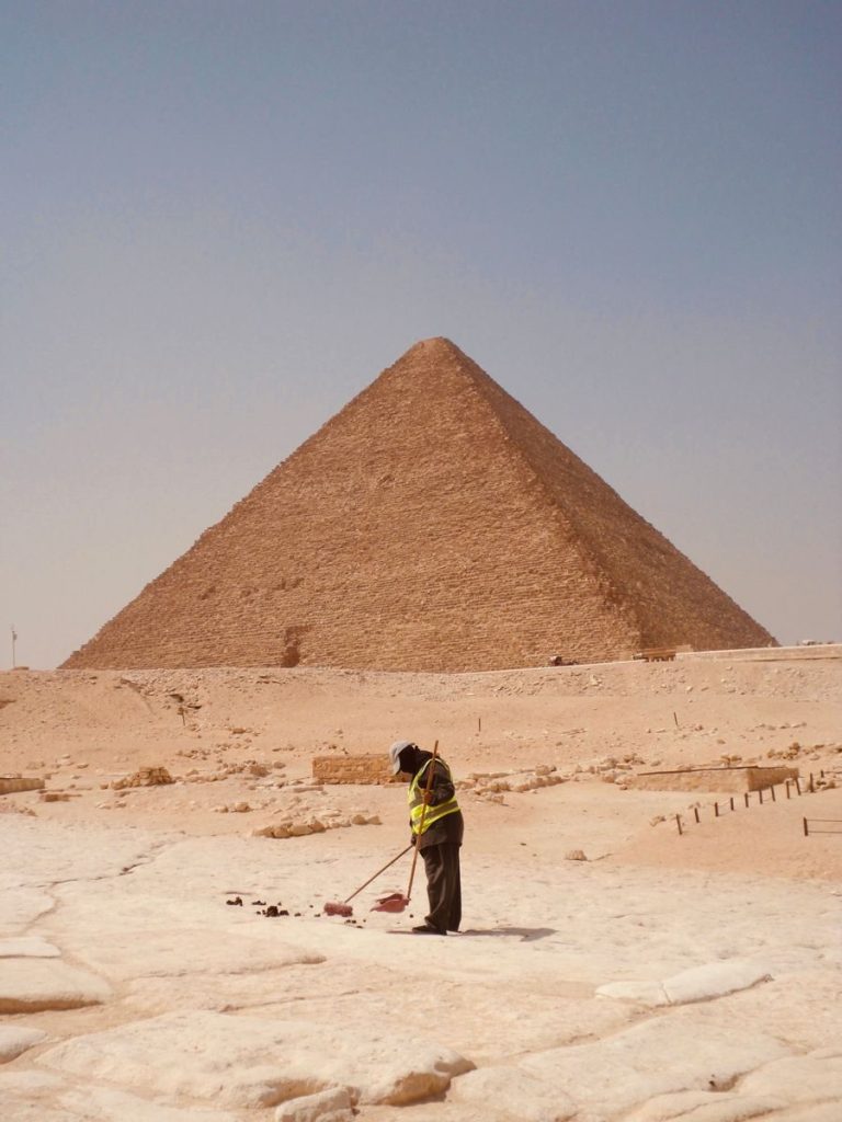 A worker cleans the area in front of the Great Pyramid of Giza, Egypt under a clear sky.