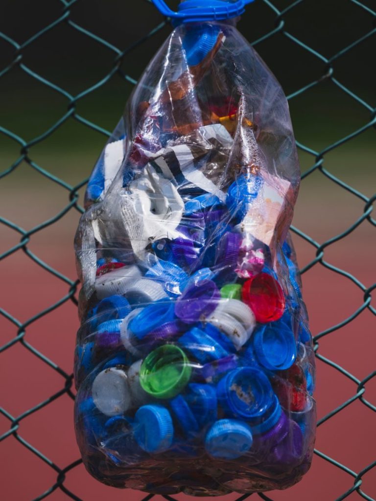 Close-up of plastic caps collected in a bag for recycling hanging on a fence.