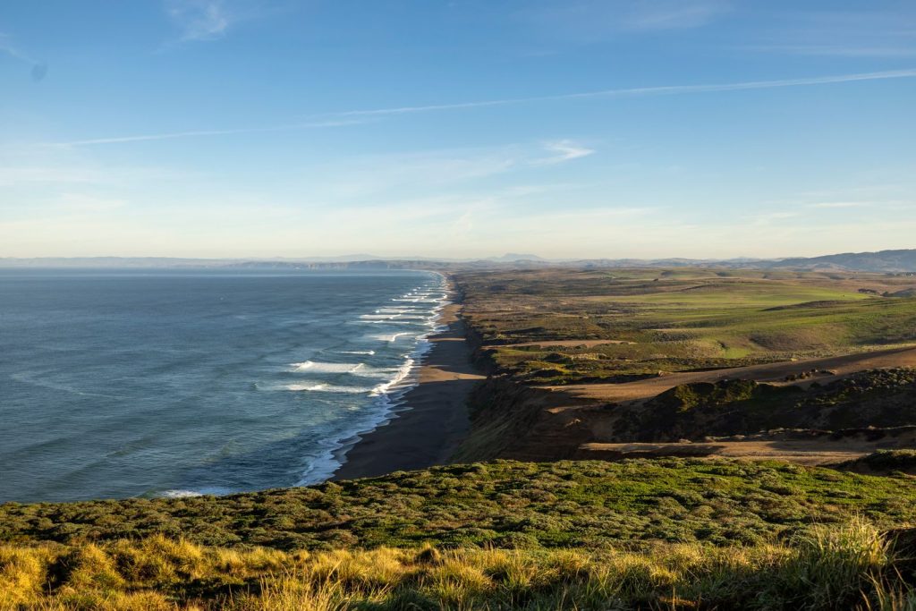 Panoramic view of a coastal landscape with waves and lush greenery under a clear sky.