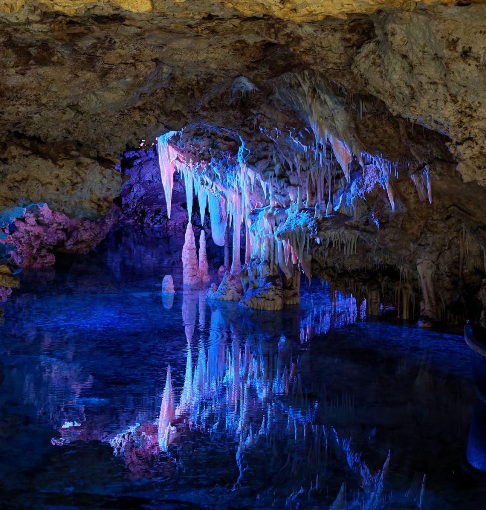 A stunning illuminated cave with stalactites and a serene reflecting pool, showcasing vibrant colors.