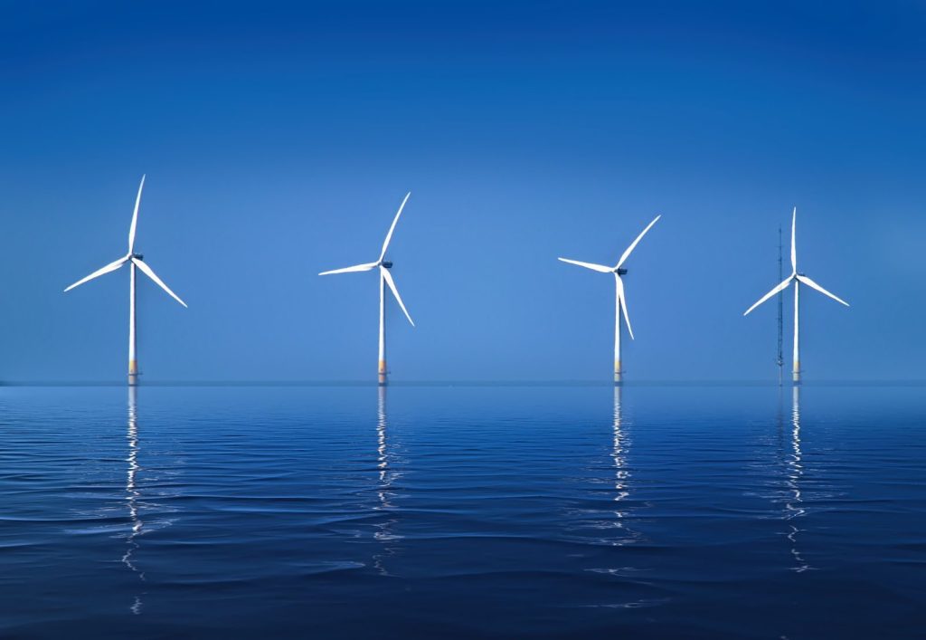Serene landscape of offshore wind turbines reflecting on calm ocean water.