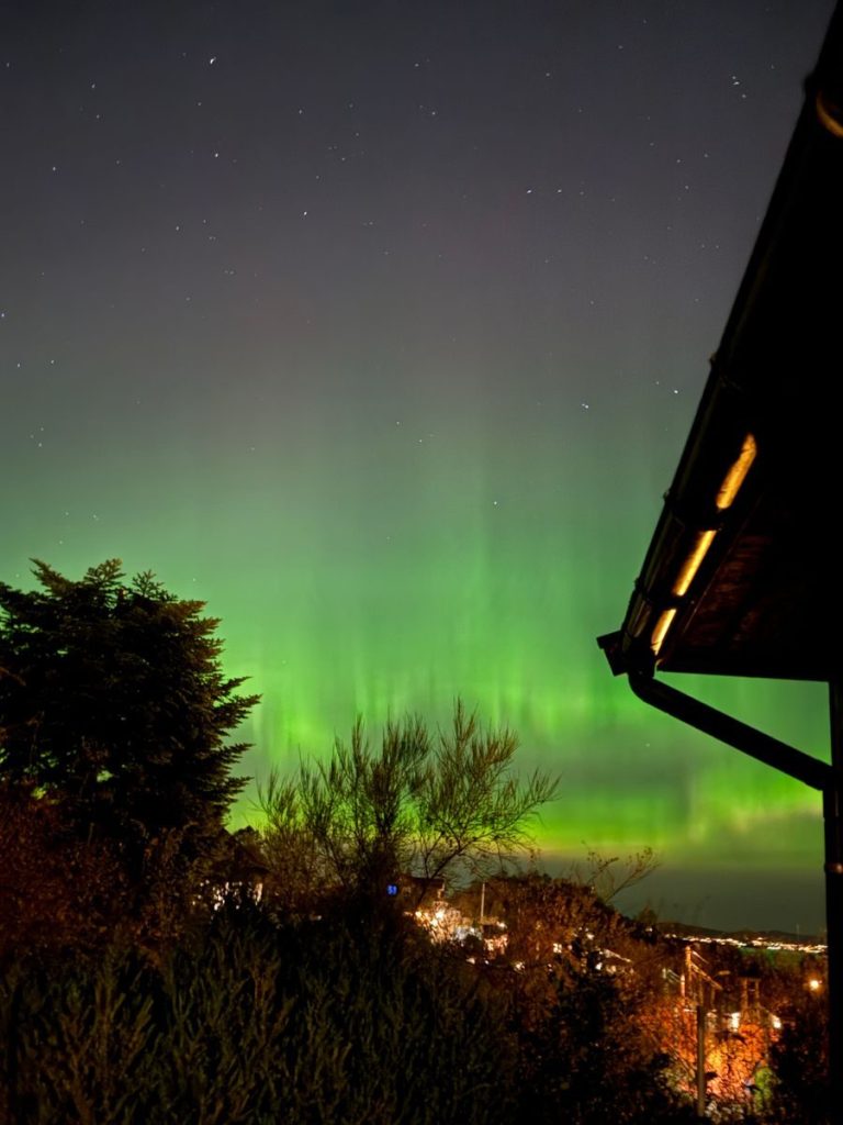 Vibrant green aurora borealis dancing over the cityscape of Bergen, Norway at night.