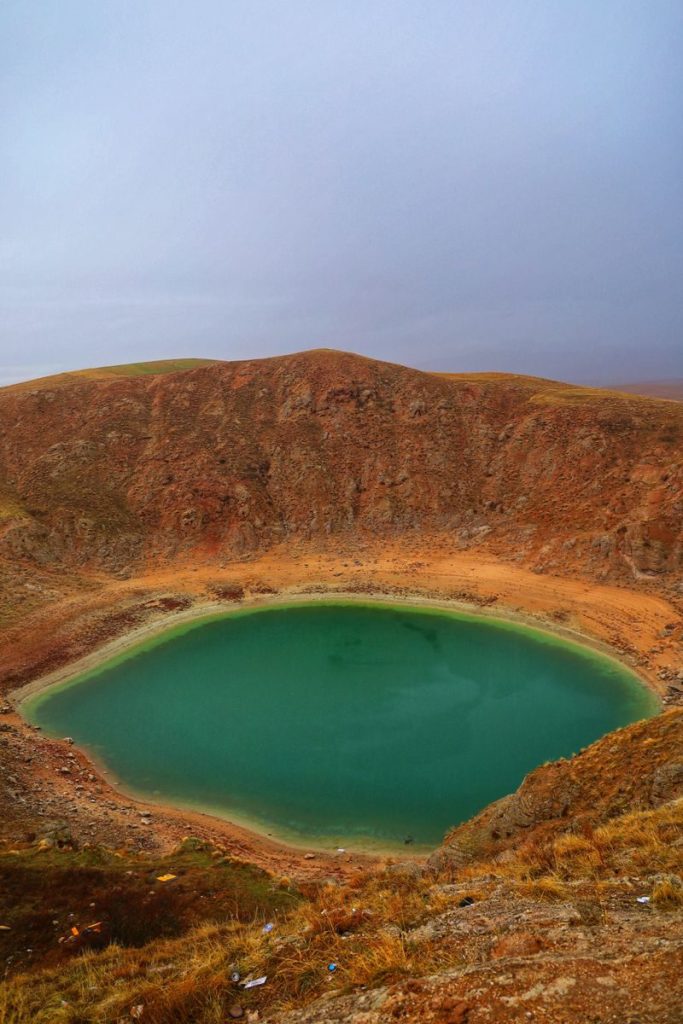 A stunning volcanic crater lake with turquoise water in a desert landscape under an overcast sky.