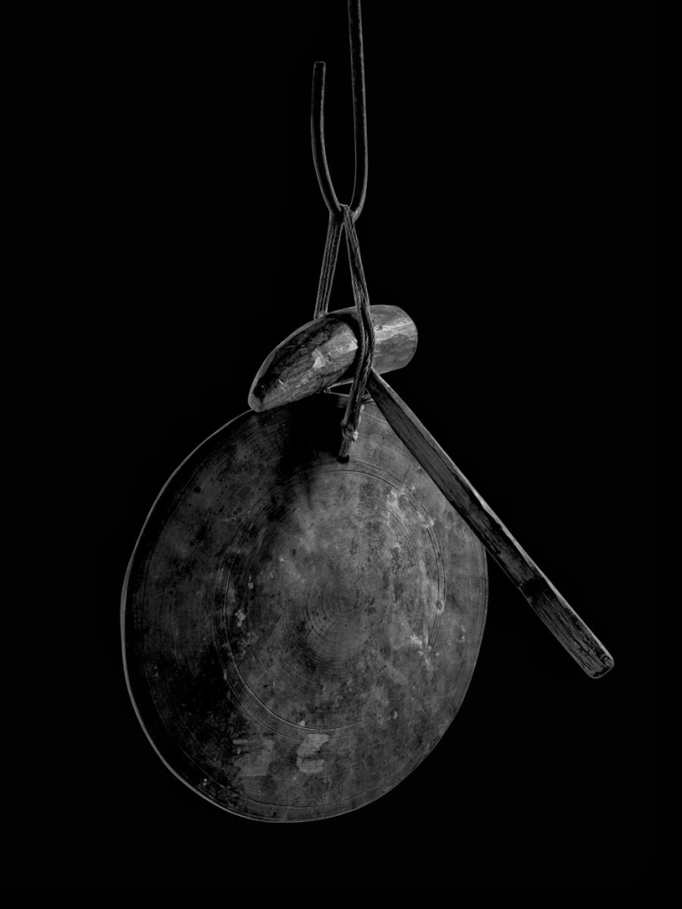 A black and white photo of a vintage gong and mallet hanging in a minimalistic style.