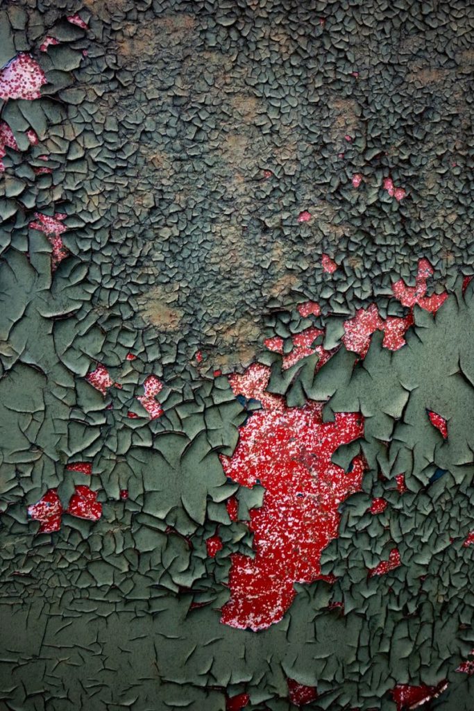 Close-up of cracked paint on a surface, featuring red and green colors, textured pattern.