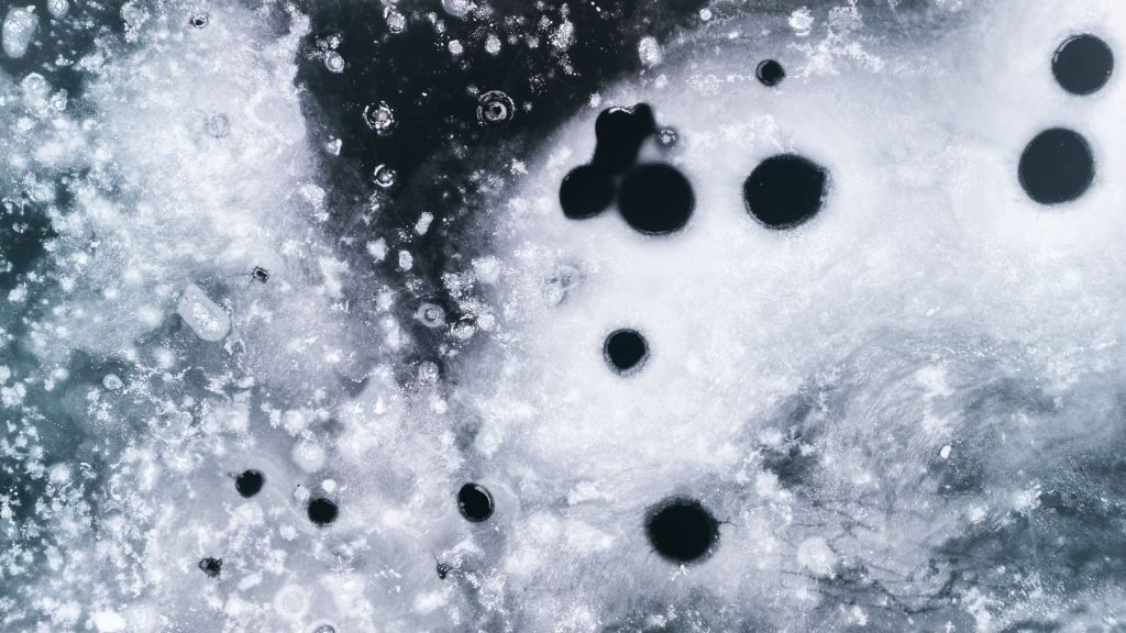 Close-up of a textured frozen ice surface with black circular formations creating abstract patterns.
