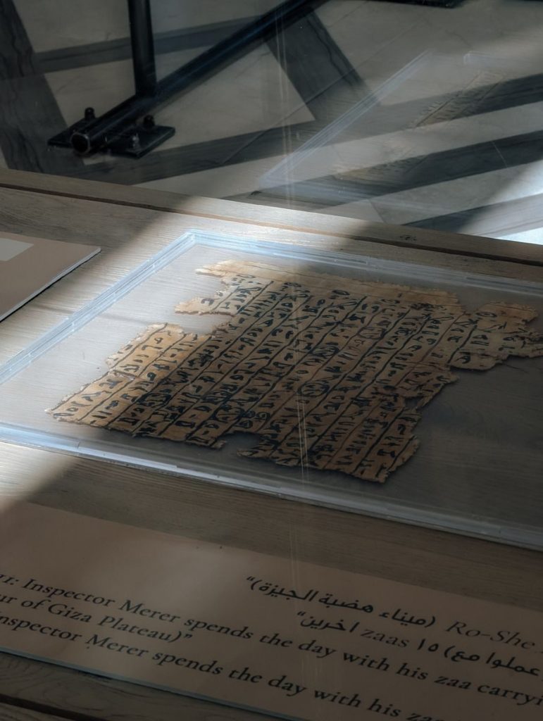A piece of ancient Egyptian papyrus on display in a Giza museum, illuminated by soft natural light.
